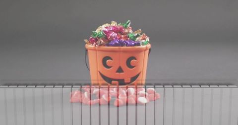 Jack-o'-lantern candy bucket overflowing with foil-wrapped treats and pink heart candies