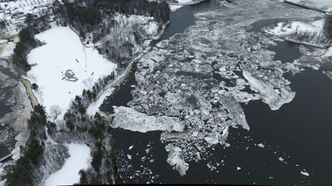 Aerial view showing icy river with drifting ice floes, snow-covered shoreline and trees