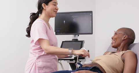 Diverse female sonographer performing abdominal ultrasound on smiling patient in clinic