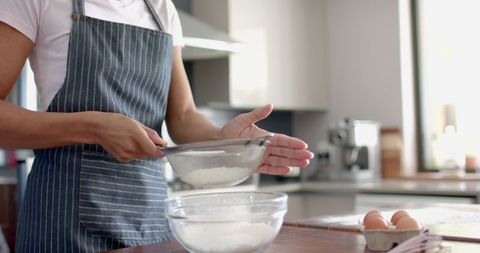 Woman Sieving Flour in Bright Kitchen for Baking Preparation