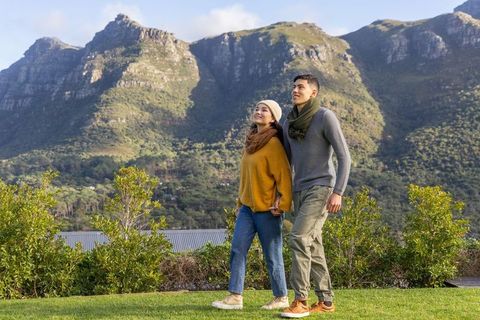 Young couple holding hands walking on green lawn with dramatic mountain foothills in autumn light
