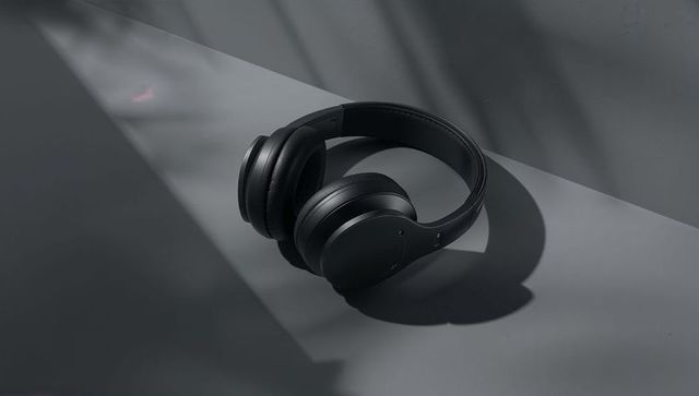 Matte black wireless over-ear headphones casting soft shadow on minimalist gray surface studio