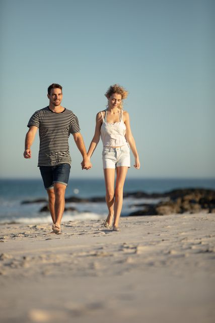 Couple walking hand in hand on beach at sunset, enjoying romantic moment. Ideal for use in travel brochures, romantic getaway promotions, relationship blogs, and lifestyle magazines. Perfect for illustrating themes of love, relaxation, and summer vacations.
