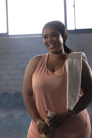 African american woman smiling holding water bottle and towel in bright gym studio