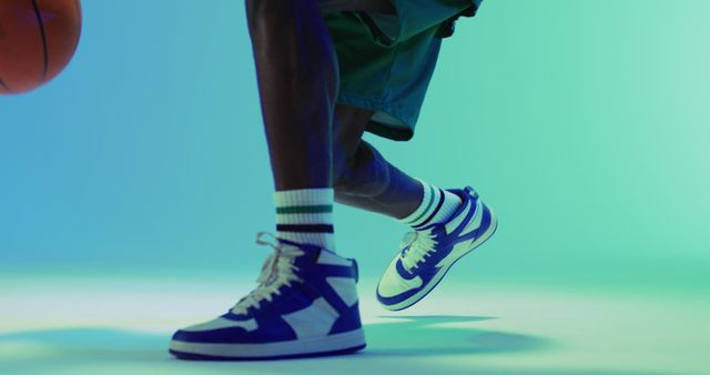 Close-up of person dribbling basketball in athletic apparel focusing on blue sneakers. Perfect for use in sports advertisements, athletic wear campaigns, fashion articles, sporting goods promotions, and dynamic lifestyle illustrations.