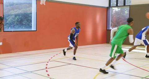 Indoor basketball fast break sprinting players passing and defending on court