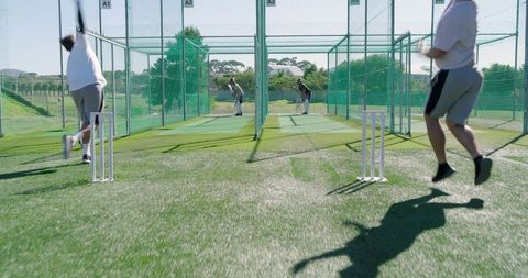 Diverse male teammates practicing cricket in outdoor nets bowling and batting training