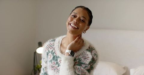 Smiling mid-adult woman relaxing on bed in cozy fuzzy sweater with smartwatch in bedroom