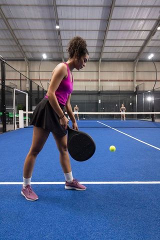 Female athlete playing padel on indoor blue court chasing bright yellow ball
