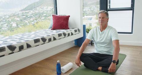 Mature man practicing yoga and checking smartwatch in bright minimalist home interior