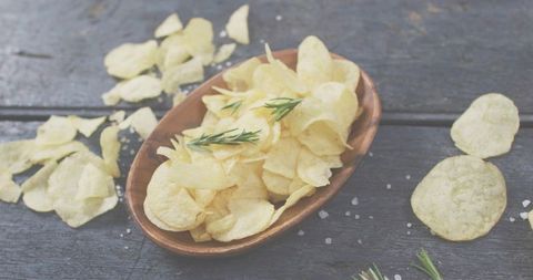 Rustic sea salt potato chips in wooden bowl garnished with fresh rosemary