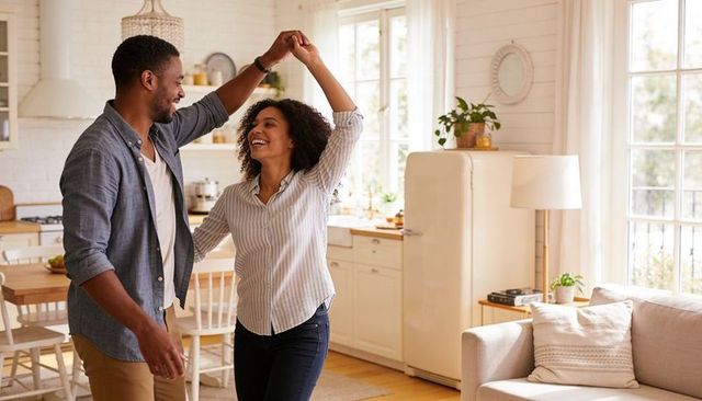 Couple twirling and laughing in sunlit cozy kitchen, celebrating everyday moments and romance