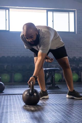 African man picking up kettlebell in gym, strength training with focus and determination