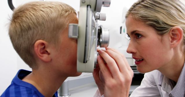 Optometrist conducting a detailed eye exam on a young boy using specialized ophthalmic equipment. The image signifies professional healthcare and routine pediatric optometry check-ups. This visual is suitable for use in health and medical websites, optometry clinic promotions, educational materials on eye care, and healthcare brochures aimed at families and pediatric care.