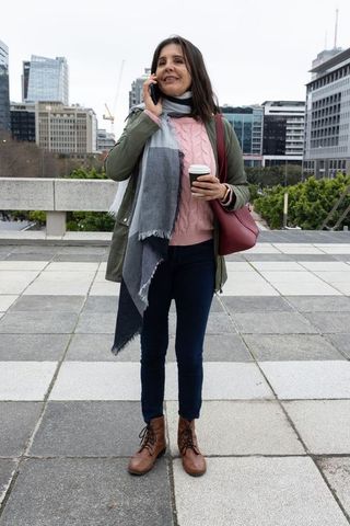 City commuter talking on phone while holding coffee and red bag, casual cold-weather outfit