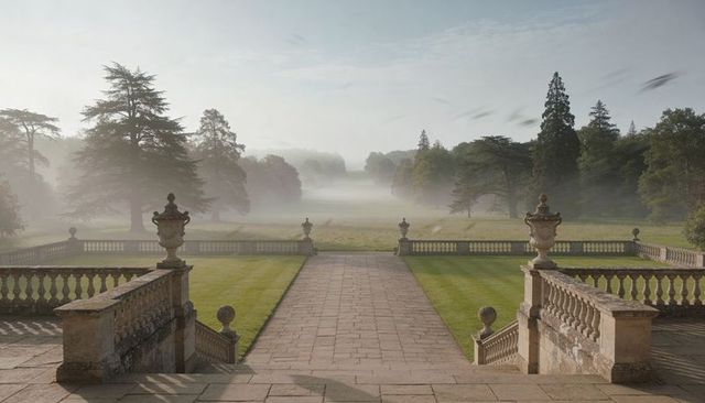 Misty manor terrace leading to symmetrical parkland with stone balustrades and urns