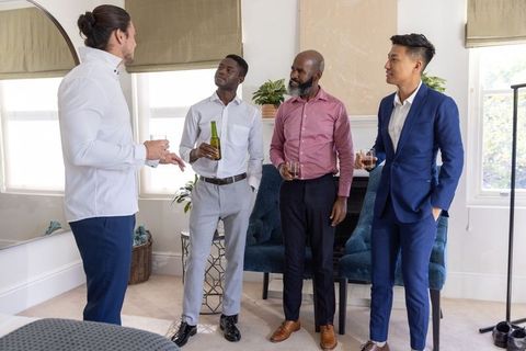 Multiethnic male colleagues chatting and networking with drinks in modern living room