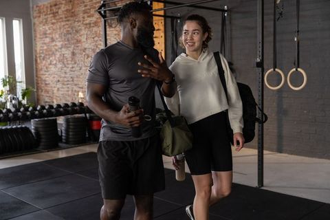 Diverse gym partners walking and chatting post-workout, carrying duffel bags and water bottles