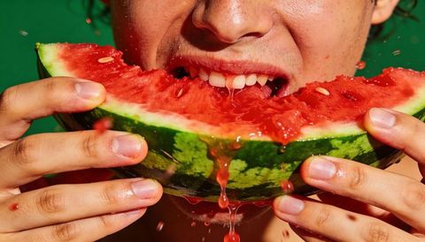 Person biting juicy watermelon wedge dripping bright red juice and seeds closeup portrait