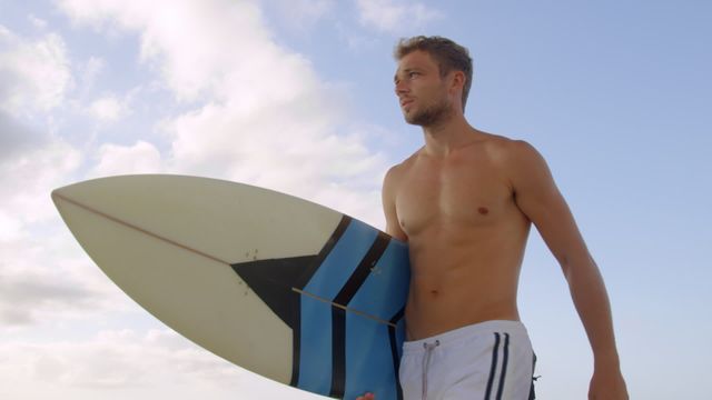 Body contour of a shirtless young man carrying a surfboard highlighted against a blue sky. Ideal for themes about surfing, beach sports, active lifestyle promotions, and summer vacation. Can be used for travel advertisements, sports magazines, and health and wellness content.