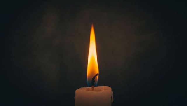 Single burning pillar candle with amber-blue flame and dripping wax on dark backdrop