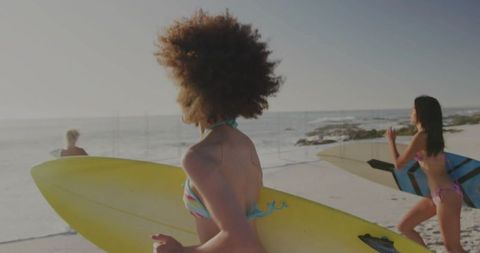 Women Holding Surfboards Running Toward Ocean on Sunny Sandy Beach at Golden Hour