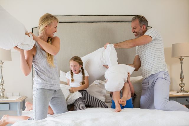 Family enjoying a playful pillow fight in a cozy bedroom. Perfect for illustrating family bonding, happiness, and indoor leisure activities. Ideal for use in advertisements, family-oriented blogs, and lifestyle magazines.