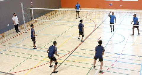 Diverse male volleyball team playing indoor gym match spiking ball over net and blocking