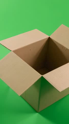 Vertical video closing in on open corrugated box on green backdrop revealing empty interior