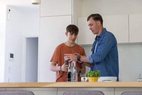 Father and teen son grinding pepper on kitchen island teaching home cooking and bonding