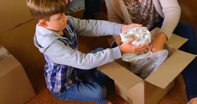 Young boy unpacking boxes with family, helping to wrap items. Perfect for articles or advertisements about family moving, teamwork, or children helping with chores.