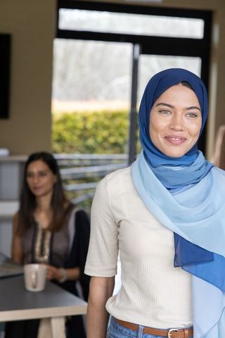 Smiling young woman wearing blue hijab collaborating with coworker in bright modern office
