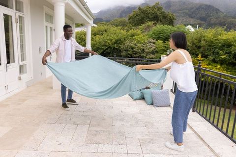 Diverse couple preparing outdoor picnic with light blue throw on spacious tiled terrace