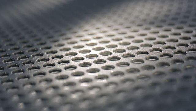 Perforated metal panel featuring diagonal rows of circular holes with dew droplets macro