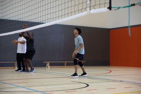 Young men preparing to block and receive volleyball on indoor court with knee pads