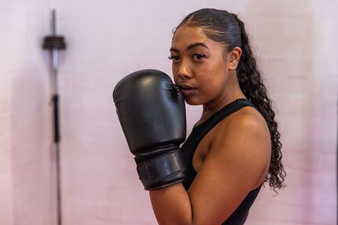 Focused asian woman boxer training in gym with black gloves and tank top