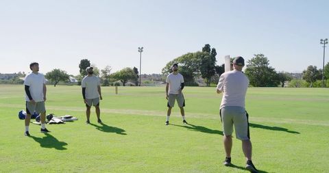 Multiracial men warming up for cricket practice on sunny grass field