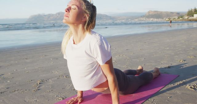 Woman practicing upward dog pose during a yoga session on the beach at sunrise, displaying fitness and connection with nature. Useful for promoting outdoor fitness, wellness lifestyles, and yoga retreats.