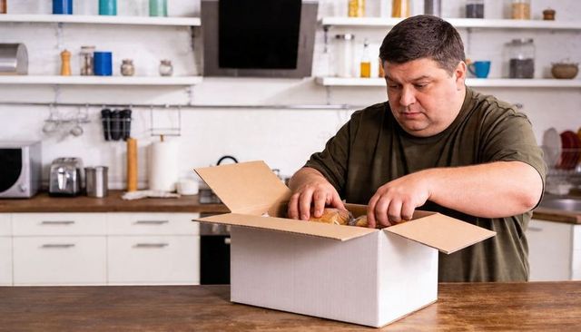Man Unpacking Grocery Box on Kitchen Counter Organizing Bread Rolls and Household Supplies
