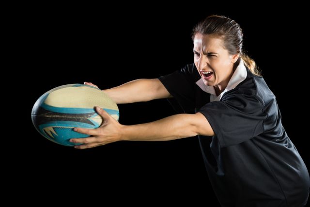 Female rugby player holding ball with determination against black background. Ideal for sports-related content, fitness promotions, teamwork concepts, and athletic training materials.