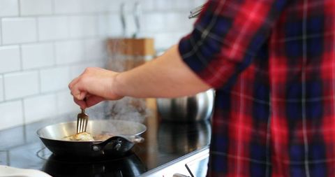 Person cooking in modern home kitchen, stirring food in frying pan