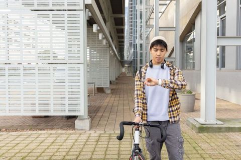 Young asian man checking smartwatch while holding road bike in modern urban corridor