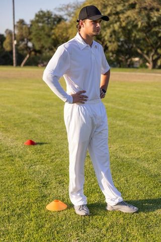 Cricket player standing hands on hips on sunlit training field with practice cones