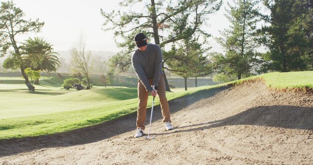 Golfer standing in sand trap ready to take shot on a sunny day. Could be used for articles or promotions related to golf, sports training, or outdoor activities.
