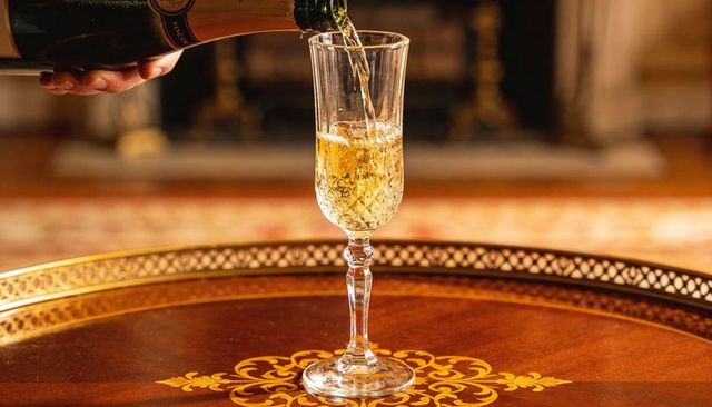 Pouring champagne into crystal flute on ornate inlaid table in elegant parlor interior