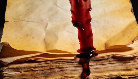 Pouring crimson liquid over aged parchment stack creating soaked stains and dripping texture