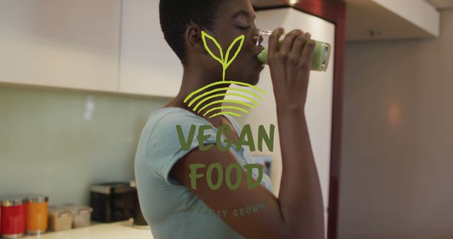 Young woman drinking a healthy green smoothie in a modern kitchen while a 'Vegan Food Locally Grown' label is displayed. Useful for promoting vegan diet, healthy living, plant-based nutrition, and sustainable food choices.