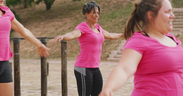 Three happy caucasian female friends in pink t shirts doing jumping jacks, training at bootcamp. Female fitness, challenge and healthy lifestyle.