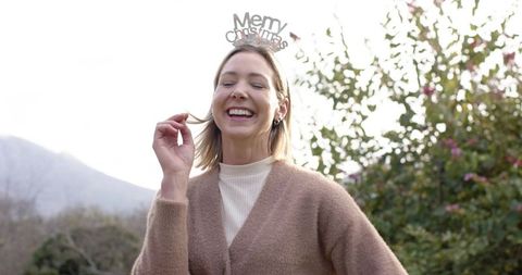 Laughing woman wearing merry christmas headband and cozy cardigan outdoors in garden