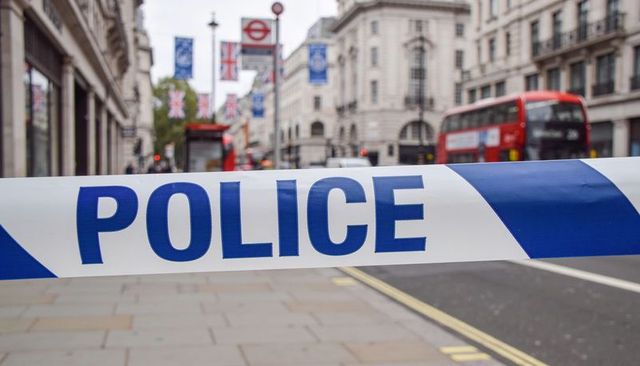 Police tape blocking london street with red double-decker bus and union jack flags